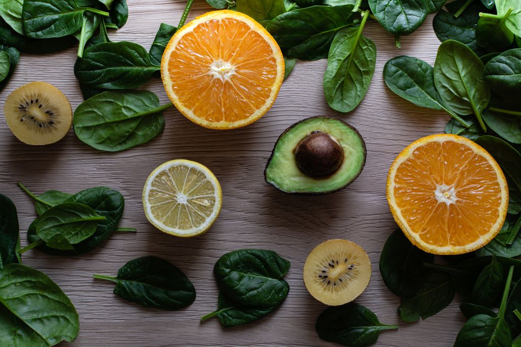Colorful flat lay of sliced fruits and fresh greens on a wooden table, ideal for healthy lifestyle concepts.