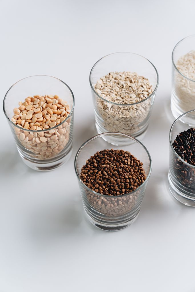 A vertical shot of various grains and seeds in glasses, showcasing raw and natural food ingredients.
